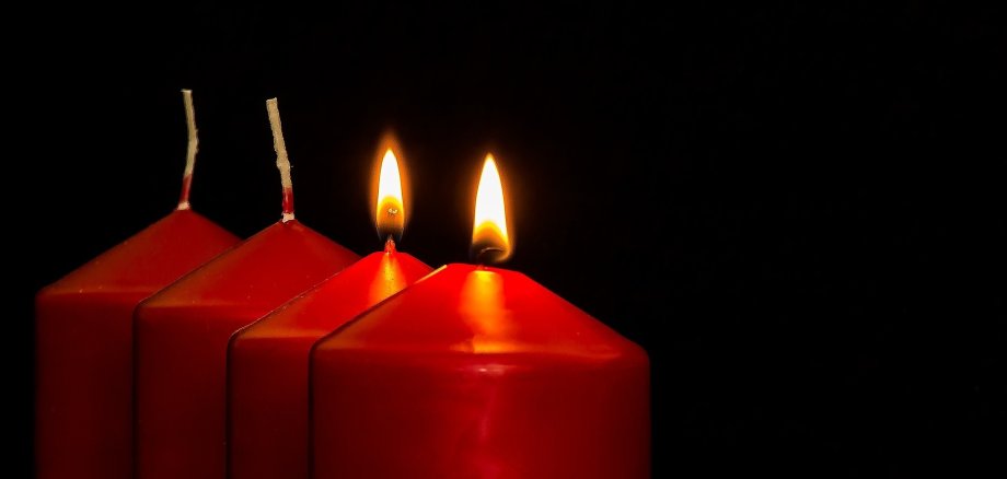 Vier Adventskerzen in rot, zwei davon brennen. 