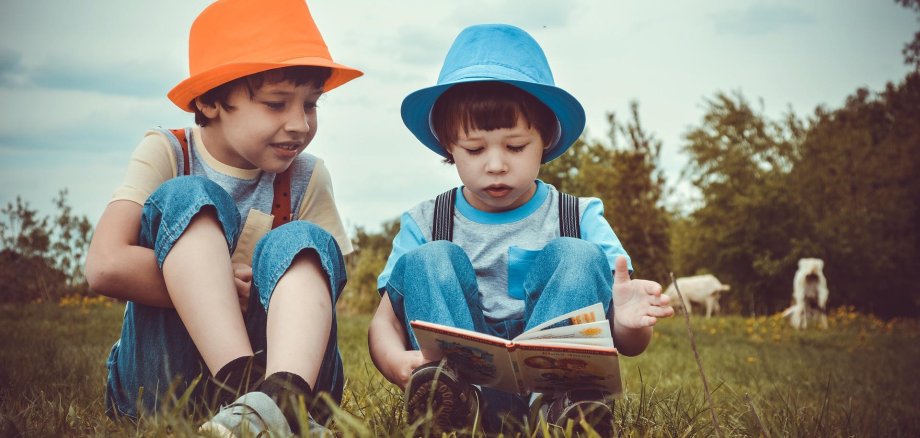 Zwei kleine Kinder mit Hüten, auf dem Rasen sitzend