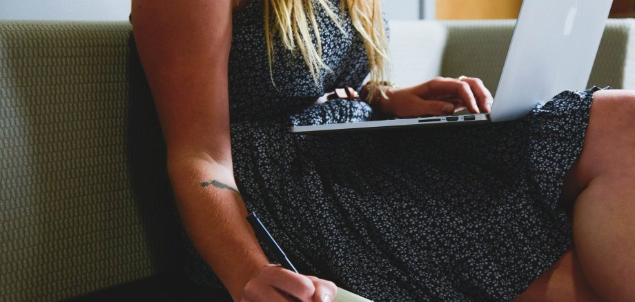 Eine Frau die am Laptop arbeitet und gleichzeitig macht handschriftliche Notizen.