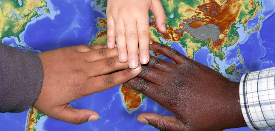 drei Kinderhände, im Hintergrund Weltkarte