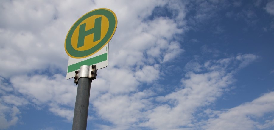 Haltestellenschild von unten fotografiert und blaue Himmel mit Wolken im Hintergrund 