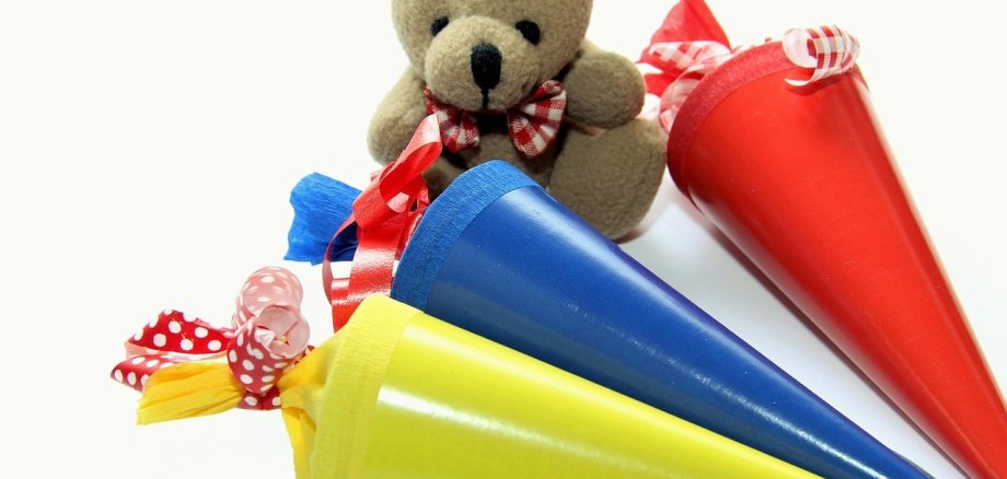 Schultuten, Zuckertüten: Gelb, blau und rot. Ein Teddy im Hintergrund. 