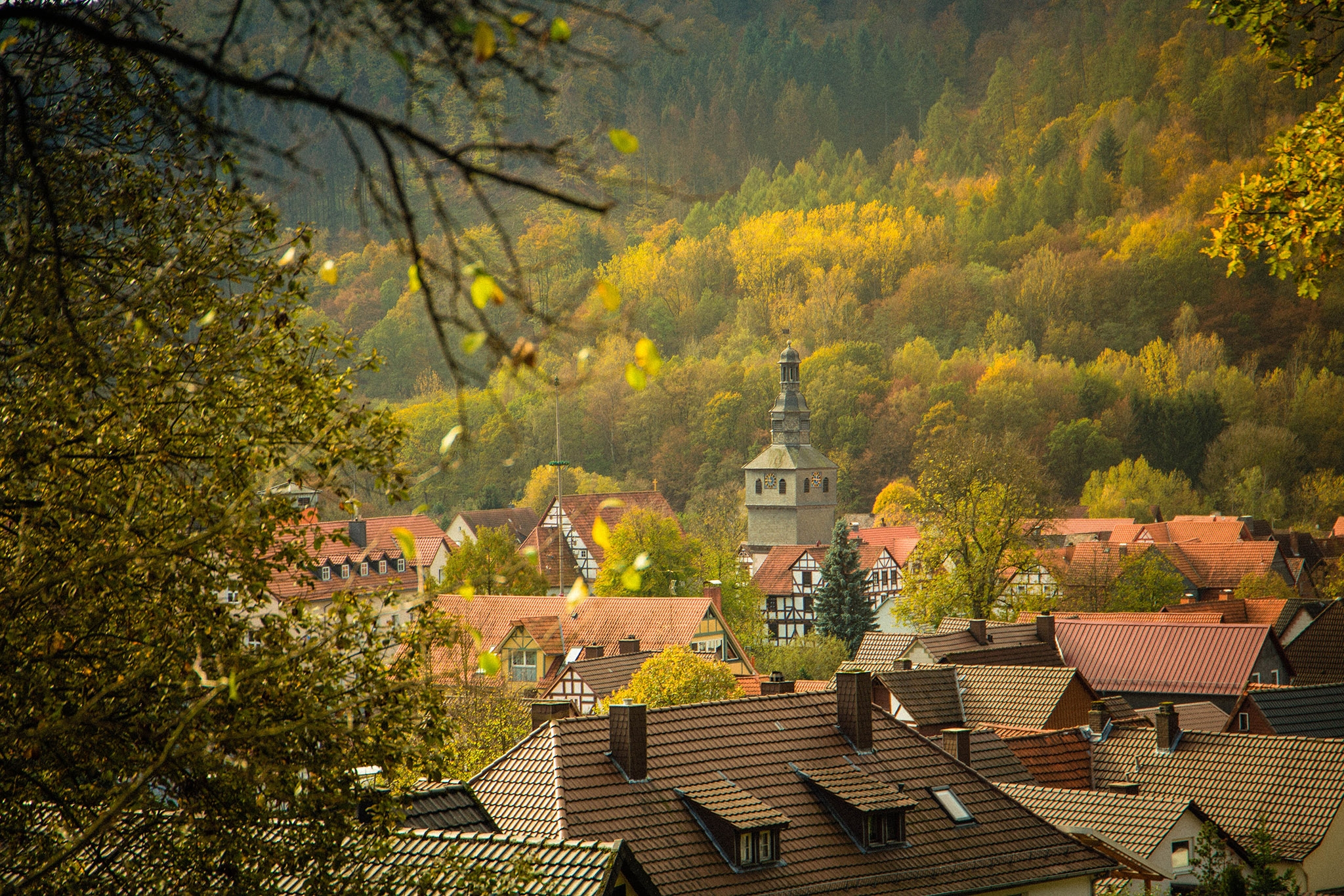 Malerische Herbstfärbung der Natur als Hintergrund für die Kirche und einige Dächer in Helsa